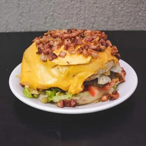 Xis coberto de cheddar derretido e bacon em cubos, com alface, tomate e ervilha